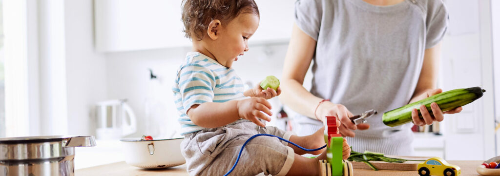 Enfant qui joue avec un bout de concombre coupé par maman